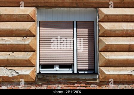 Renovated double window with white wooden frame and plastic blinds mounted on cracked dilapidated broken striped with horizontal lines old style Stock Photo