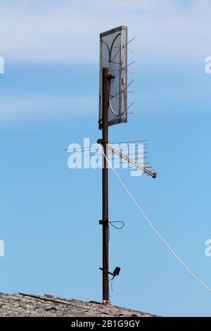 Rusted strong metal pole on top of old suburban family house with mounted small box like and two large different types of TV antennas on clear blue Stock Photo