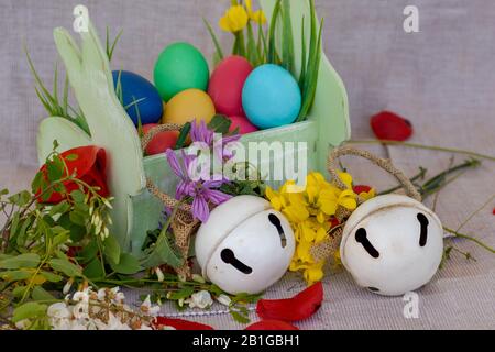 Easter composition with a basket of dyed Easter eggs, spring flowers and two white bells Stock Photo
