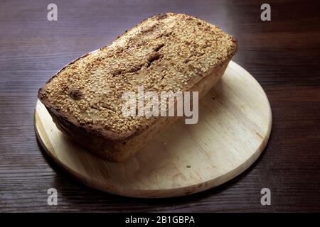 Freshly baked buckwheat bread. A loaf of bread lies on a round kitchen board on a brown wooden table. Gluten-free healthy home-made product. Natural Stock Photo