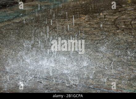 raindrops falling in a torrential downpour on a pavement during heavy weather in the wet winter causing flooding. Stock Photo