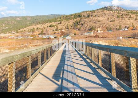 Looking across wooden trestle bridge on Kettle Valley Rail Trail to view of vineyards and mountains in autumn Stock Photo