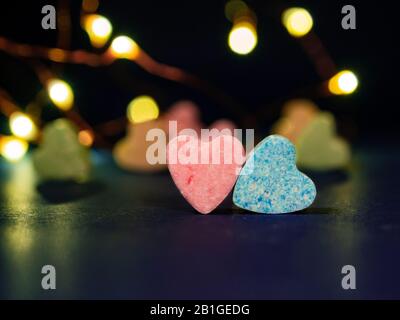 Two heart-shaped candies. Pink and blue hearts in focus and few candies in various colors on blurry background. Concept of Valentine's Day, or diet su