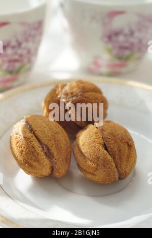 Cookies in the form of walnuts on a white saucer. Background two tea cups on a sunny table. Stock Photo