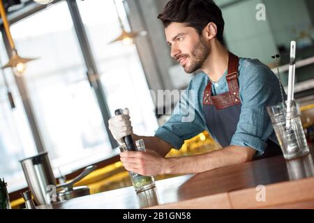 Drink Preparation. Bartender standing at counter near the window squeezing out lime juice thinking smiling happy Stock Photo