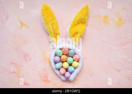 Pastel and gold colored eggs and bunny ears on a pink background. Easter celebration concept. Top view, flat lay, copy space Stock Photo
