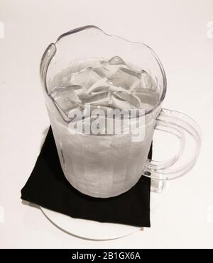 Pitcher with cold water and ice cubes on table napkin. Stock Photo