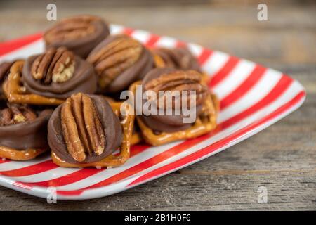 close up of pecan nut and melted chocolate on salty pretzel on red and white striped plate Stock Photo