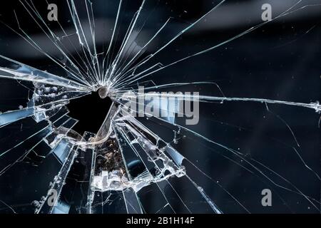 Closeup of a broken window. Cracks radiate from the break, and there is an irregular hole near the center. Stock Photo