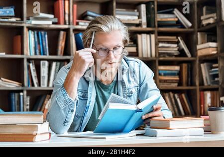 Focused young man study library desk read book hold pen education concept Stock Photo