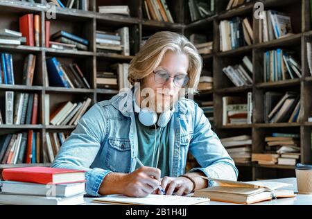Concentrated bearded young man glasses sit library write essay education concept Stock Photo
