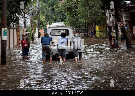 People pushing a stranded car through a flooded road.Heavy rains triggered widespread flood in Jakarta inundating thousand homes. Stock Photo