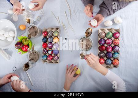 human hands of 4 sorbian women are writing with melting wax on the white surface of the egg on a Table with colorful painted easter eggs. Stock Photo