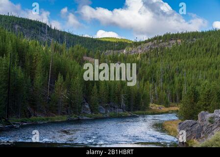 River curving through green forested mountains under a bright blue sky with white fluffy clouds. Peaceful and relaxing location in the countryside. Stock Photo