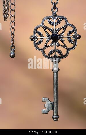 An old antique metal key hangs on a silver chain against a light background Stock Photo