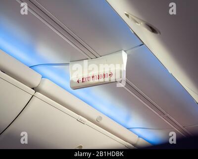 Emergency exit sign in airplane. Word red color in Thai language mean exit way on sign hanging on ceiling for passenger in cabin economy class on the Stock Photo