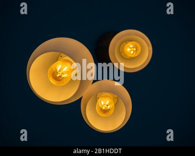 Three round modern ceiling lights hanging from ceiling from bottom view in dark blue room. Stock Photo
