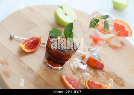 Two cocktails of whiskey with cola and grapefruit with ice vodka and mint. On a wooden board, fragments of fruit are flung up. Photo with depth of Stock Photo