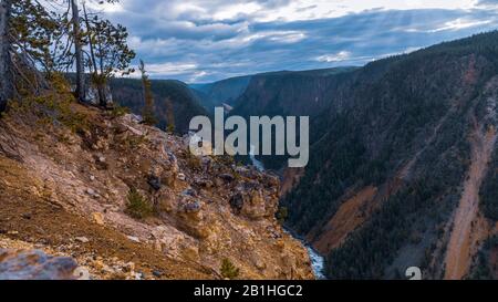 Looking down and across a very deep and colorful canyon with a river in the bottom, cloudy skies above. Stock Photo