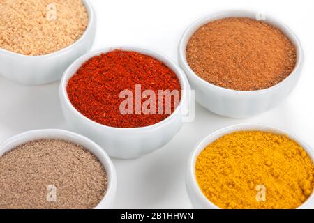 Different spices in white bowls isolated on white background. Paprika, Curry, Black Pepper, Ginger, Cinnamon, Bay Leaves. Stock Photo