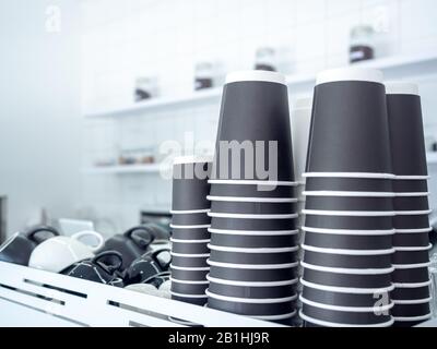 Black paper coffee cups stacked in a pile. Row of black paper cups upside down on shelf on white cafe background with copy space. Stock Photo