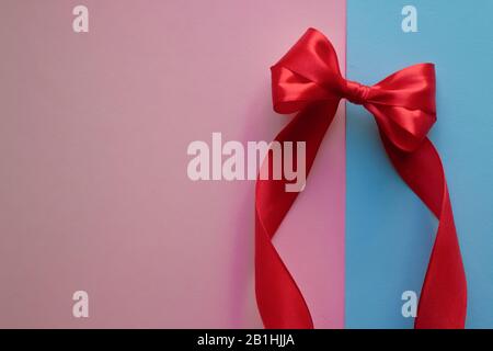 Bright red bow made from silk and satin ribbon on blue and pink background. Festive concept with copy space. Birthday greetings concept. Stock Photo