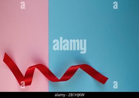 Red silk ribbon twisted on blue and pink background. Festive concept with copy space. Top view. Stock Photo