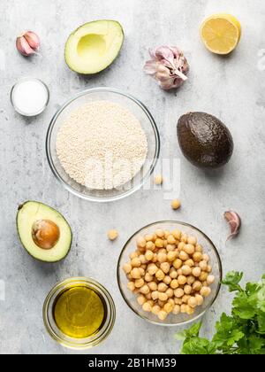 Hummus ingredients, chickpeas, garlic cloves, olive oil, lemon half, salt and avocado. Top view food. Grey background. Stock Photo