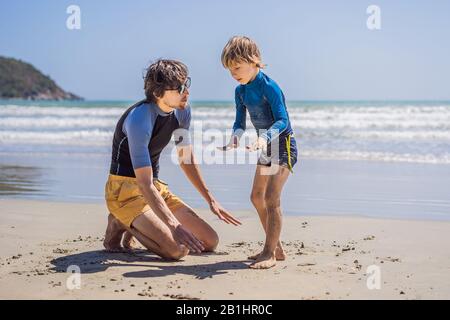 Father or instructor teaching his son how to surf in the sea on vacation or holiday. Travel and sports with children concept. Surfing lesson for kids