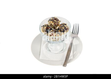 four balls Ice cream dessert, vanilla flavor, with chocolate topping in nuts, isolated on a white background in creamer on a plate with a spoon and a Stock Photo