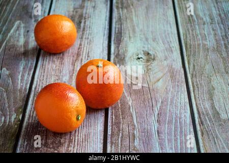 Three red oranges lie on a wooden table Stock Photo