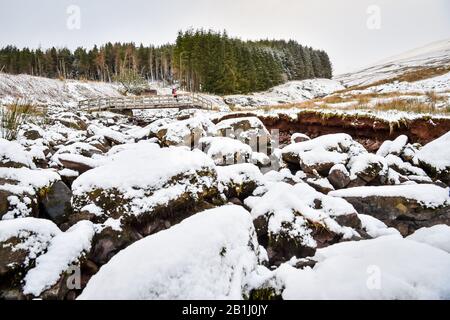 A walker crosses a bridge over a stream on the footpath towards Pen y Fan mountain on Brecon Beacons National Park, Wales, after temperatures plummeted overnight across Britain, and forecasters warned of more ice and snow over the next 24 hours. Stock Photo