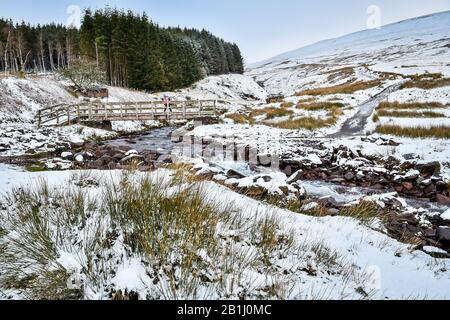 A walker crosses a bridge over a stream on the footpath near Pen y Fan mountain on Brecon Beacons National Park, Wales, after temperatures plummeted overnight across Britain, and forecasters warned of more ice and snow over the next 24 hours. Stock Photo