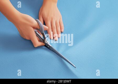 Top view on the hands of a professional tailor woman who cuts blue fabric with scissors Stock Photo