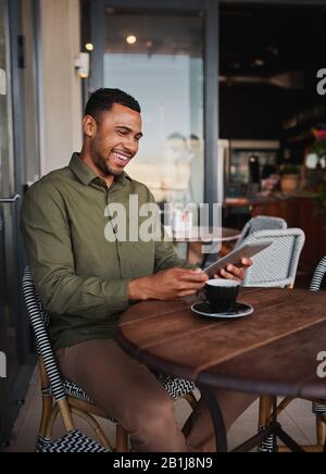 Happy young afro-american man using digital tablet in office cafeteria while drinking coffee Stock Photo