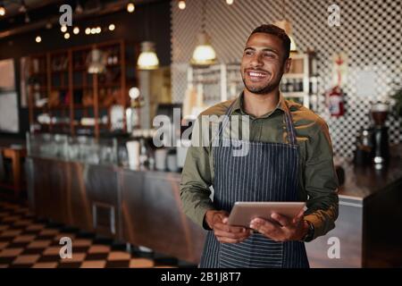 Cheerful young male owner holding digital tablet while standing in cafe Stock Photo