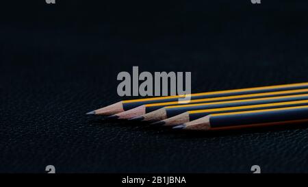 Five black pencils with an orange stripe lying in a row one after another diagonally on a black background Stock Photo