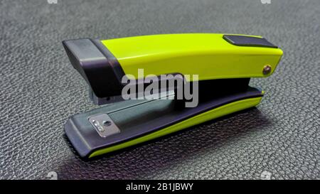 One green color stapler standing on a black leather surface Stock Photo