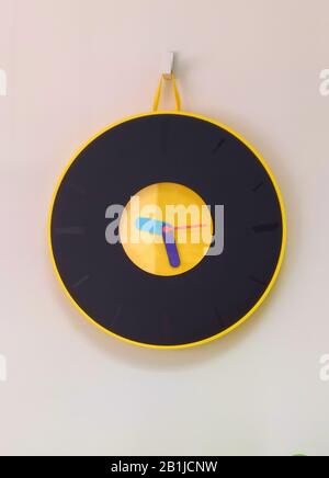 Black wall clock with a yellow contour hanging on a hook on a white wall Stock Photo