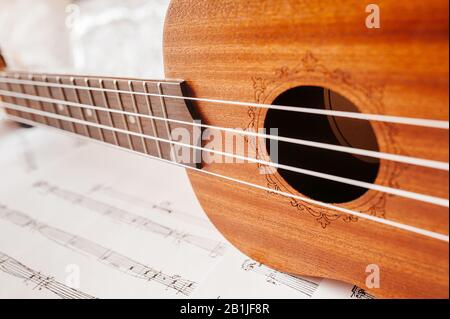 The neck of a traditional ukulele guitar. Ukulele with white nylon strings on the background of musical notes. Lifestyle , mood toning. Stock Photo