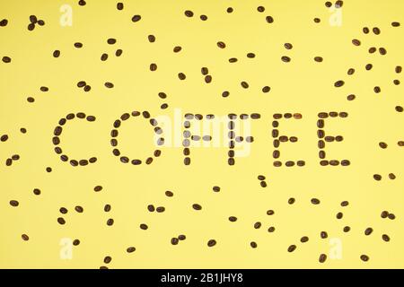 Coffee word made from fresh roasted arabica coffee beans on yellow background. Creative minimal flat lay Stock Photo