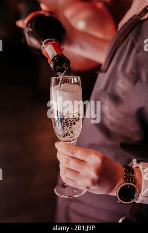 waiter without a face holds a glass and a bottle in his hands, pours champagne with bubbles into a glass Stock Photo