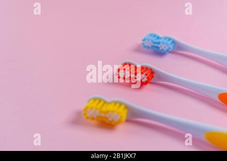 Three bright toothbrushes on a delicate pink background. Red, yellow, blue. Family relationship concept Stock Photo