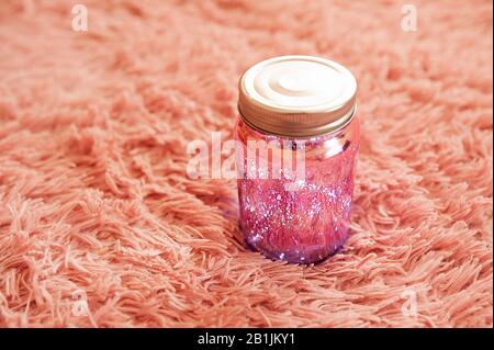 sparkle magic electric pink jar with LED bulbs inside and a silver closed lid on a fluffy, high-pile pink blanket. Stock Photo