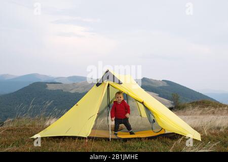 Small kid in yellow tent in spring mountains. Travel with child concept Stock Photo