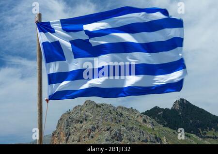 Greek flag waving in the wind close-up on the background of mount Tsambika (Rhodes, Greece) Stock Photo