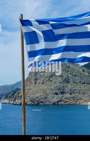 Greek flag waving in the wind close-up on the background of mount Tsambika vertical orientation (Rhodes, Greece) Stock Photo