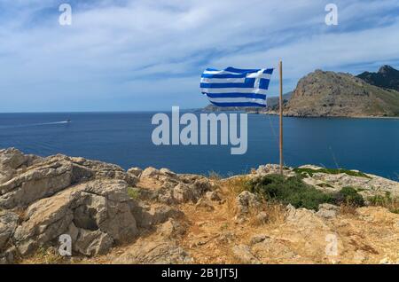 Beautiful Mediterranean landscape with a Greek flag on the rocky coastline and Tsampika mountain  in the distance (Rhodes, Greece) Stock Photo