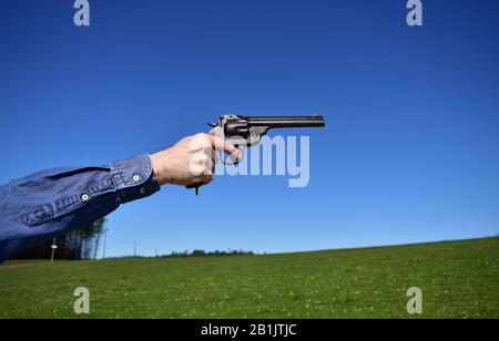 Man holding a .44 or .45 caliber revolver outdoors with blue sky. Stock Photo