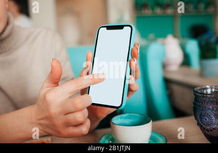 woman's hand with a French manicure holds a mint and black phone against the background of a table in a cafe with blue porcelain cups. Business meetin Stock Photo
